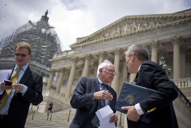 Sanders speaks with an aide following an outdoor address where he denounced legislation that would allow for cuts to pension plan benefits in order to shore up the plan's finances. Sanders was well-received but the loud cheers of his supporters disturbed a nearby prayer circle for the Charleston shooting victims; many reporters called the event an 