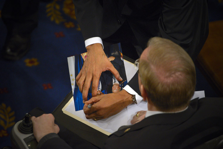 Following his 2015 State of the Union speech and after spending several minutes shaking hands on the House floor, President Barack Obama is pulled aside by an aide. A man asks the President to autograph a photo of him posed with a much younger looking Obama.